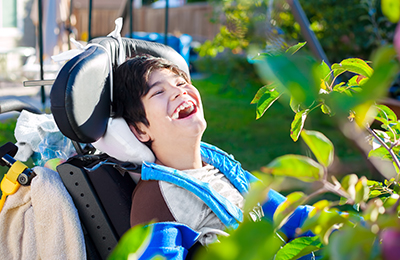 Boy sitting in a wheelchair lauging outdoors.